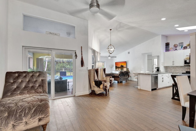 living room with high vaulted ceiling, sink, ceiling fan with notable chandelier, and light hardwood / wood-style flooring