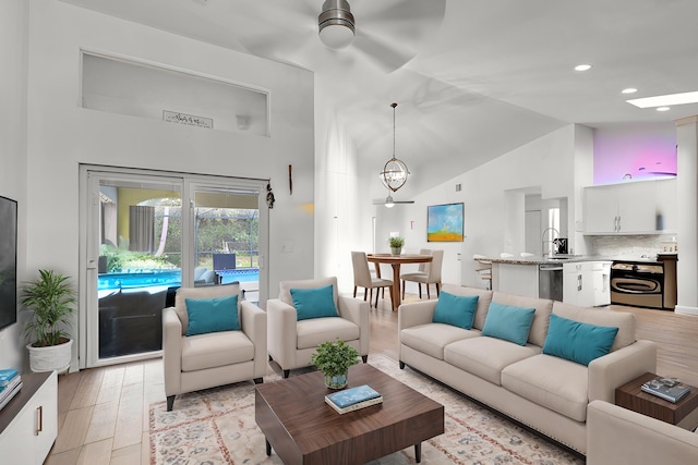 living room featuring ceiling fan with notable chandelier, light hardwood / wood-style flooring, sink, and high vaulted ceiling