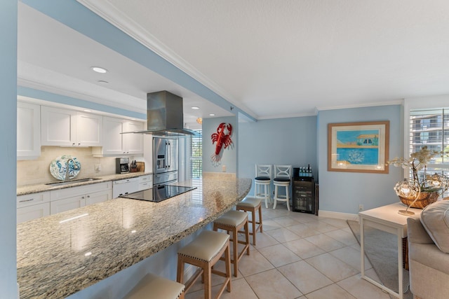 kitchen with island exhaust hood, light stone counters, white cabinets, a breakfast bar, and tasteful backsplash