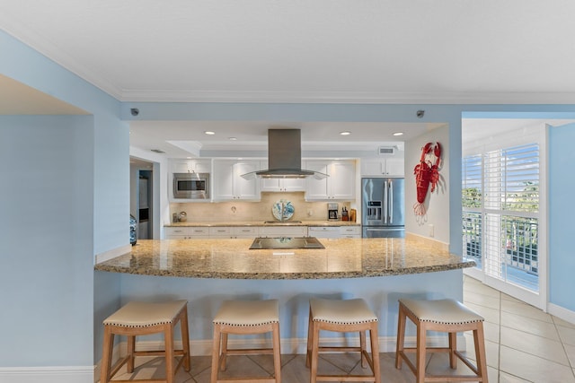 kitchen with island exhaust hood, appliances with stainless steel finishes, white cabinets, tasteful backsplash, and a kitchen bar