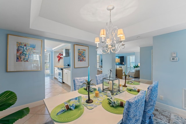 dining space with light tile floors, a tray ceiling, and an inviting chandelier