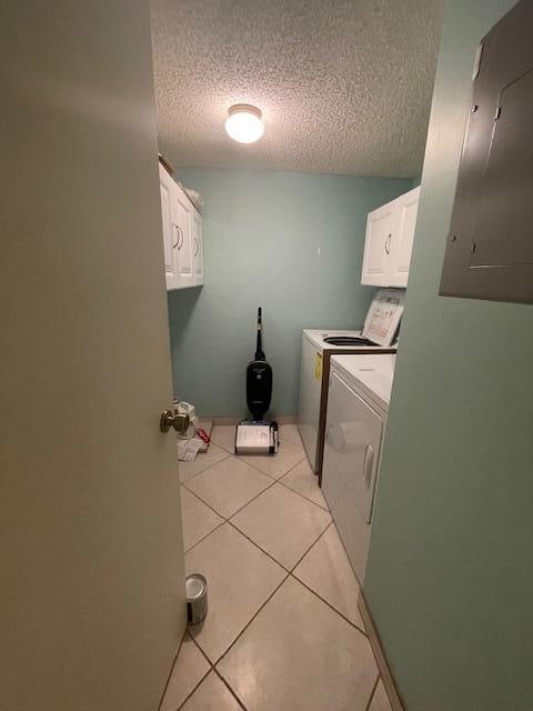 washroom with a textured ceiling, light tile patterned floors, cabinets, washing machine and clothes dryer, and electric panel