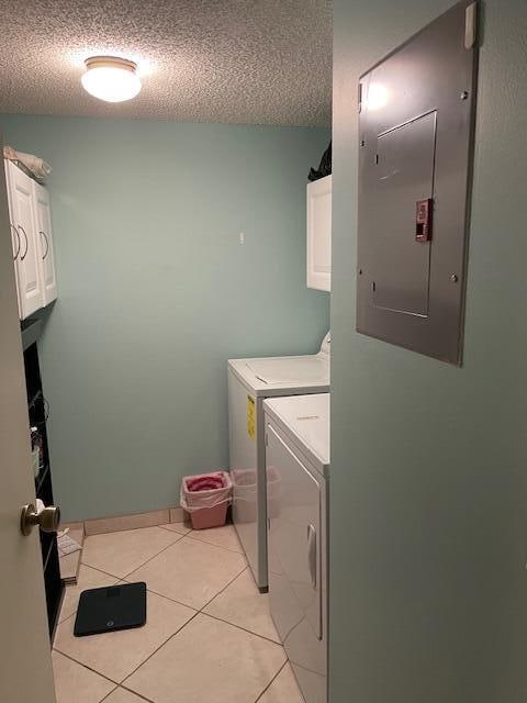 clothes washing area with a textured ceiling, electric panel, cabinets, light tile patterned flooring, and washing machine and dryer