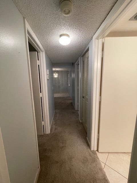 corridor with a textured ceiling and light colored carpet