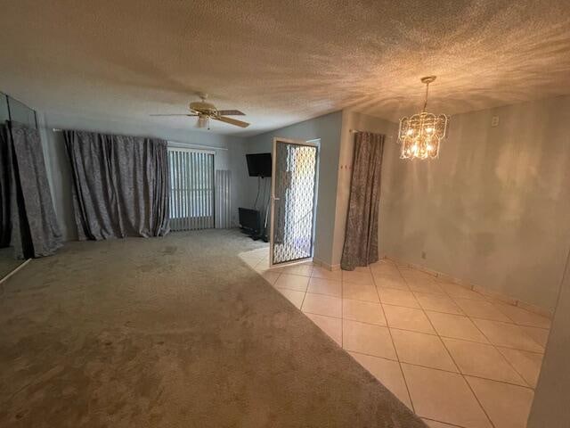 carpeted spare room featuring ceiling fan with notable chandelier and a textured ceiling