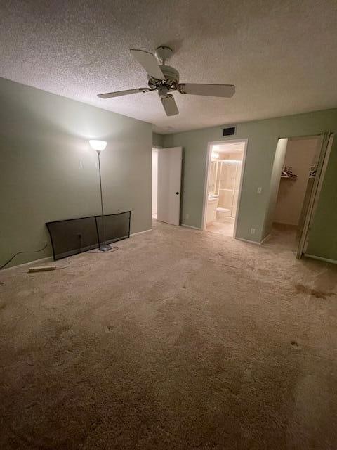 unfurnished bedroom featuring ceiling fan, a textured ceiling, a walk in closet, and light colored carpet