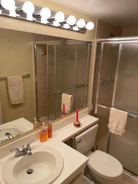 bathroom featuring toilet, vanity, and a shower with shower door