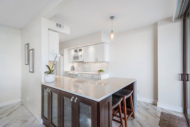 kitchen with hanging light fixtures, light tile flooring, white cabinets, tasteful backsplash, and a breakfast bar area