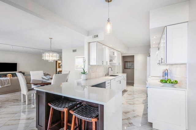 kitchen featuring backsplash, a kitchen breakfast bar, a notable chandelier, and white cabinets