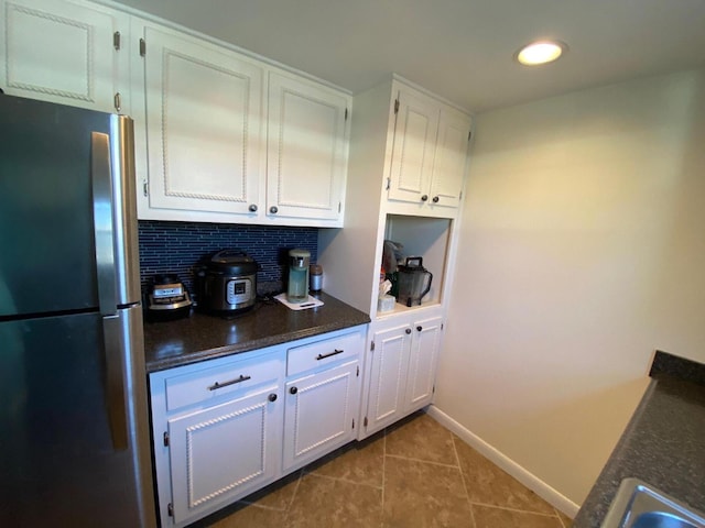 kitchen with backsplash, stainless steel fridge, tile floors, and white cabinetry