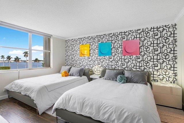 bedroom featuring a water view, a textured ceiling, ornamental molding, and dark wood-type flooring