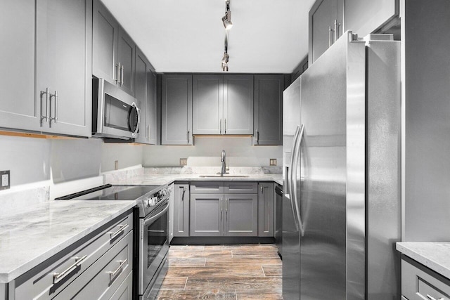 kitchen with stainless steel appliances, gray cabinetry, track lighting, light wood-type flooring, and sink