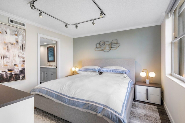 bedroom featuring crown molding, rail lighting, ensuite bathroom, wood-type flooring, and a textured ceiling