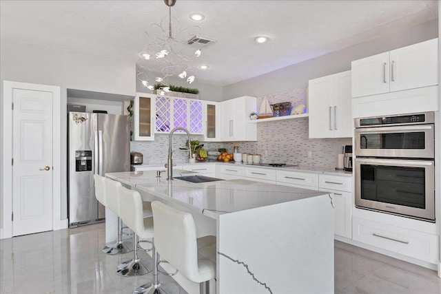 kitchen with pendant lighting, light stone counters, appliances with stainless steel finishes, a chandelier, and white cabinetry