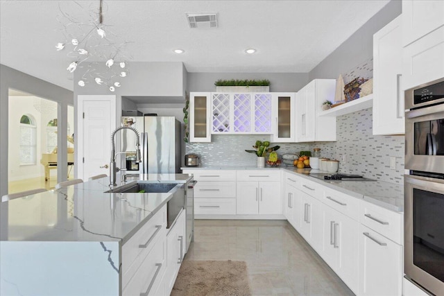 kitchen featuring a kitchen island with sink, light stone counters, stainless steel appliances, light tile flooring, and white cabinetry