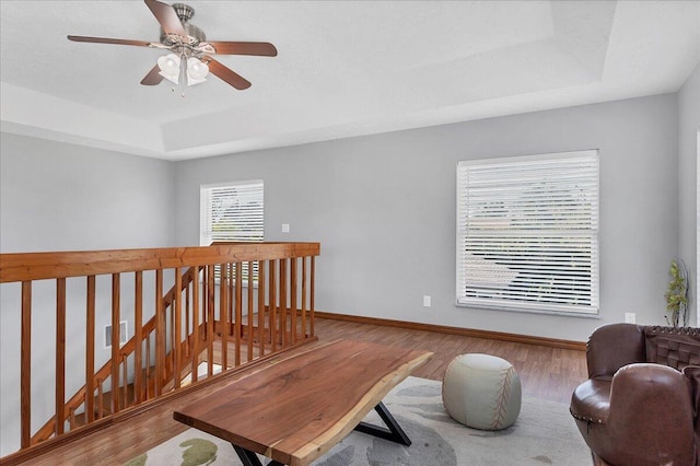 living room with a raised ceiling, wood-type flooring, and ceiling fan