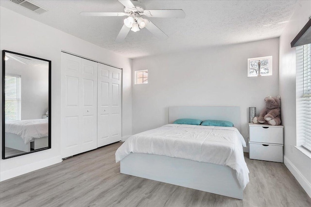 bedroom with light hardwood / wood-style floors, a textured ceiling, a closet, and ceiling fan