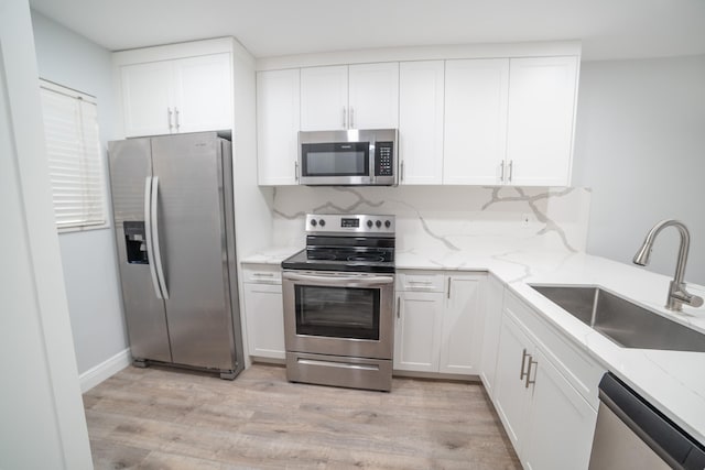 kitchen featuring sink, light stone counters, appliances with stainless steel finishes, light hardwood / wood-style flooring, and white cabinetry