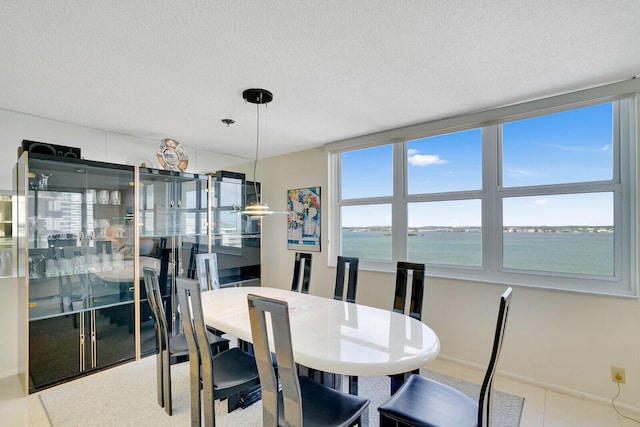 dining area featuring light tile flooring, a water view, and a textured ceiling