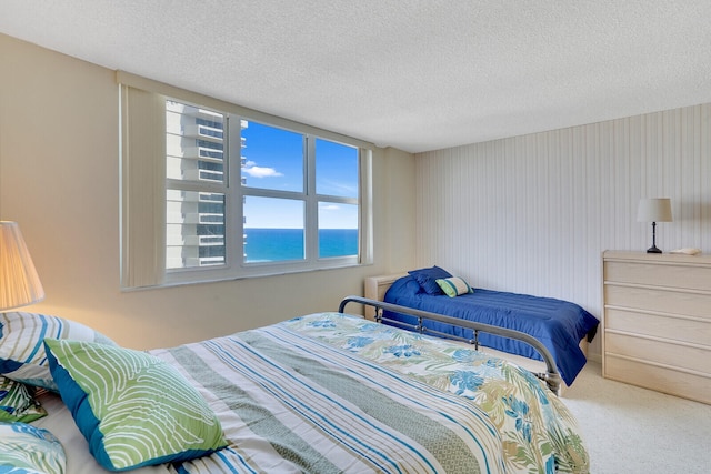 bedroom featuring a water view, light colored carpet, and a textured ceiling