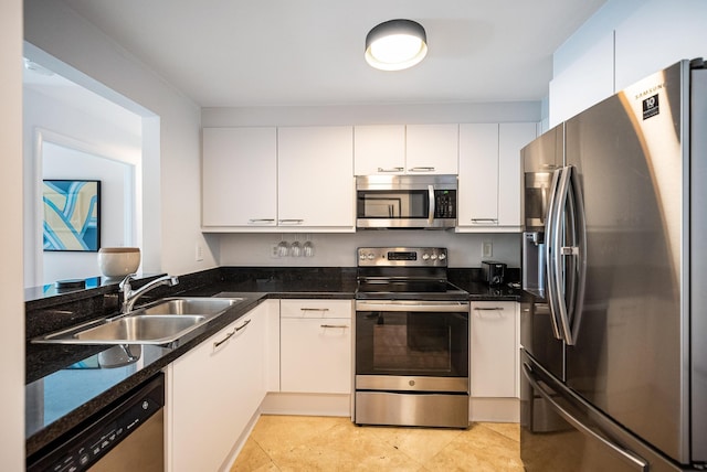 kitchen featuring dark stone counters, stainless steel appliances, sink, light tile patterned floors, and white cabinets