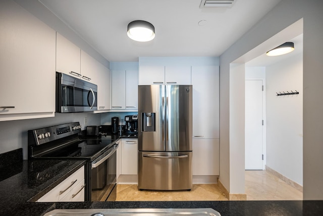 kitchen featuring white cabinets, appliances with stainless steel finishes, light tile patterned floors, and dark stone countertops