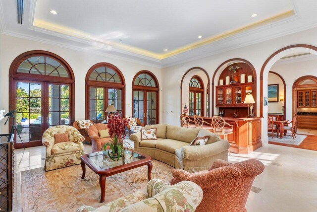 living room featuring light tile flooring, a raised ceiling, ornamental molding, and french doors