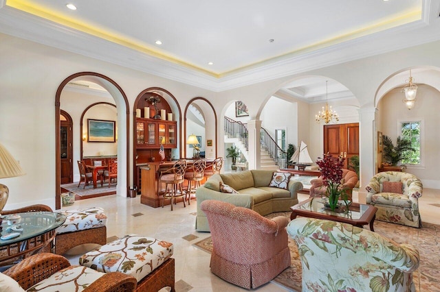 tiled living room featuring an inviting chandelier, a tray ceiling, ornate columns, and ornamental molding