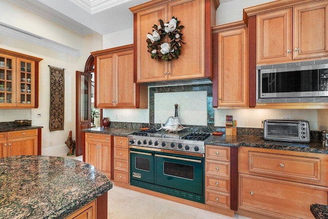 kitchen with backsplash, dark stone countertops, stainless steel microwave, and double oven range