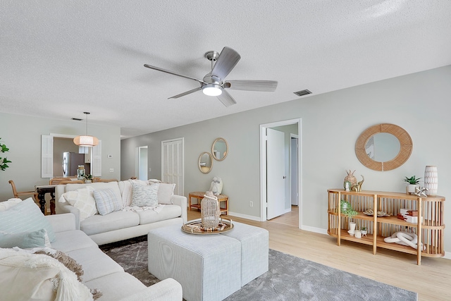 living room featuring a textured ceiling, light wood-type flooring, and ceiling fan