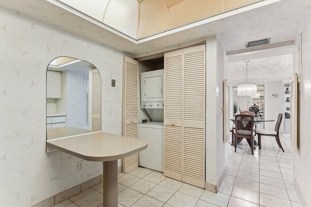 interior space featuring light tile patterned floors, stacked washer and dryer, and a notable chandelier