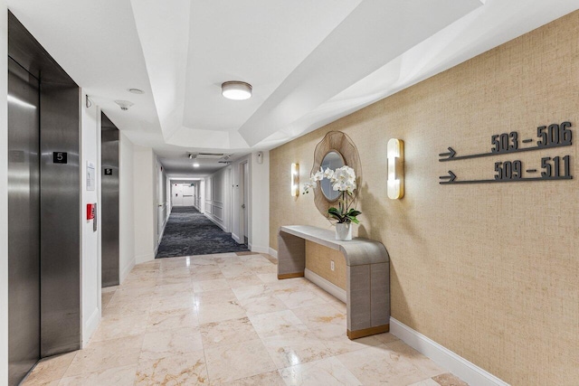 hallway with elevator and a raised ceiling