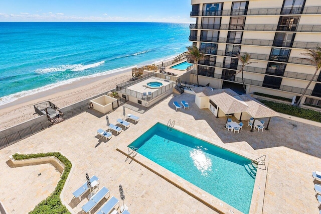 community pool featuring a patio area, fence, a beach view, and a water view