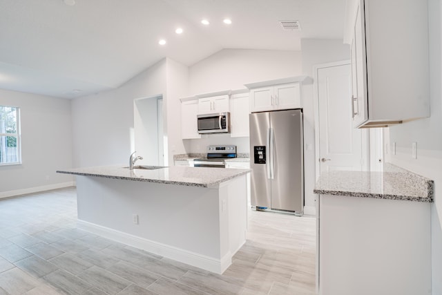 kitchen with light stone counters, lofted ceiling, stainless steel appliances, sink, and white cabinetry