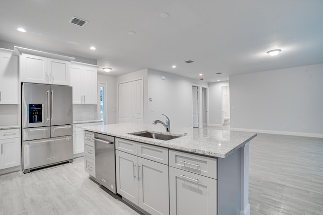 kitchen featuring light stone countertops, a center island with sink, appliances with stainless steel finishes, white cabinets, and sink