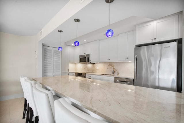 kitchen featuring hanging light fixtures, light stone countertops, stainless steel appliances, and white cabinets