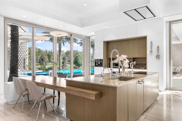 kitchen featuring sink, a raised ceiling, decorative light fixtures, white cabinetry, and light wood-type flooring