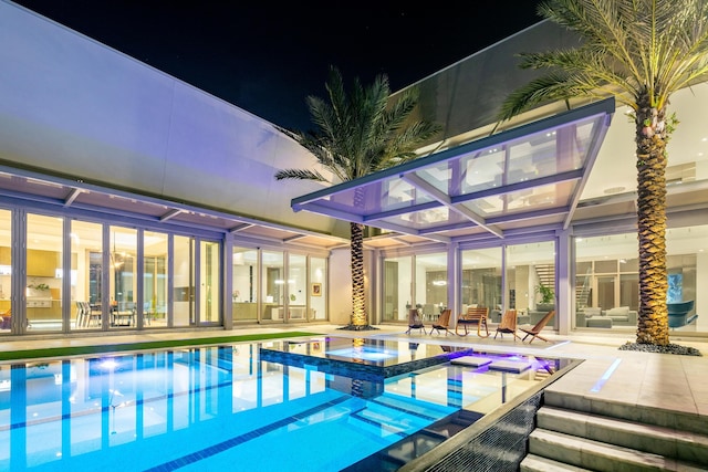 pool at night featuring a patio and an in ground hot tub