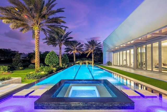 pool at dusk with a patio and an in ground hot tub