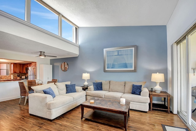 living room featuring a towering ceiling, wood-type flooring, a textured ceiling, and ceiling fan