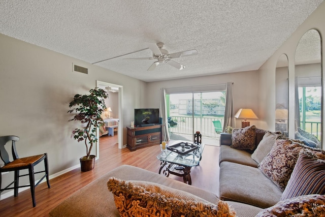 living room with ceiling fan, a textured ceiling, and light hardwood / wood-style floors