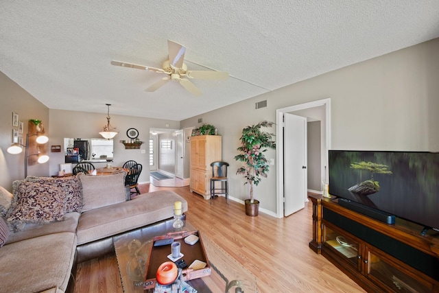 living room featuring a textured ceiling, ceiling fan, and light wood-type flooring