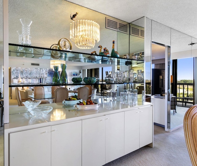 bar featuring light carpet, an inviting chandelier, hanging light fixtures, a textured ceiling, and white cabinetry