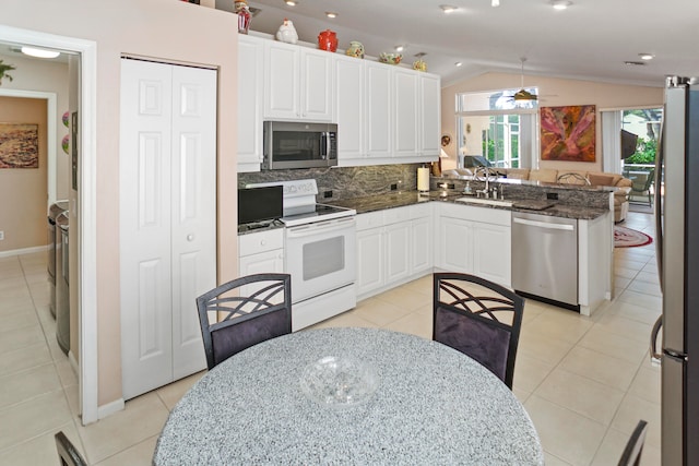 kitchen with kitchen peninsula, vaulted ceiling, light tile patterned flooring, white cabinetry, and stainless steel appliances