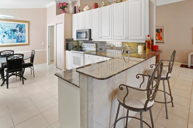 kitchen featuring white cabinets, a kitchen breakfast bar, decorative backsplash, white electric range oven, and kitchen peninsula