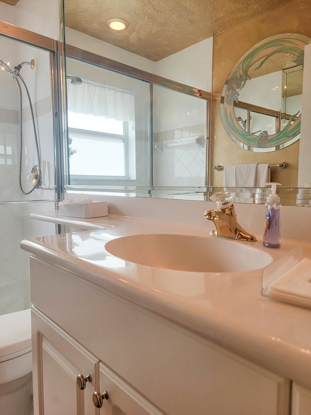 bathroom with a shower with door, vanity, a textured ceiling, and toilet