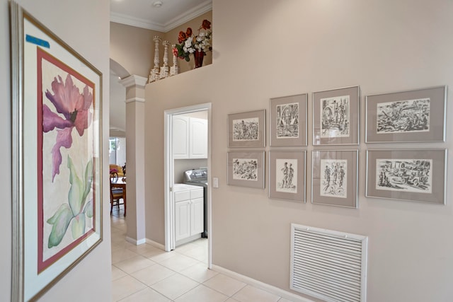 corridor featuring decorative columns, crown molding, a high ceiling, washer / clothes dryer, and light tile patterned flooring