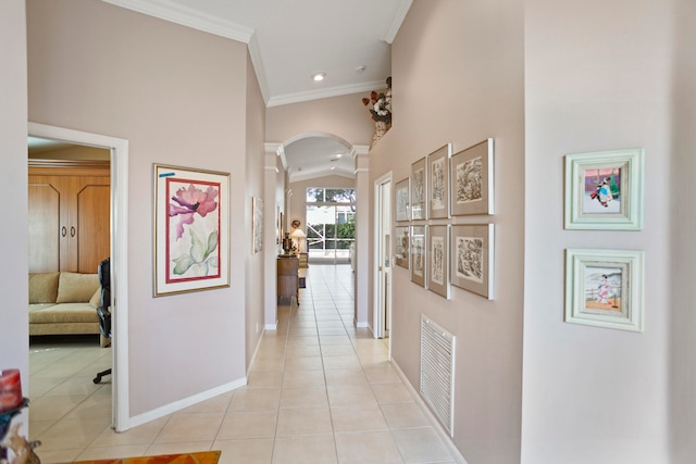 hallway with light tile patterned floors, ornamental molding, a towering ceiling, and decorative columns