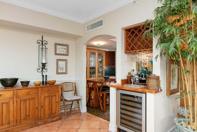 bar featuring a textured ceiling, wine cooler, ornamental molding, and light tile floors