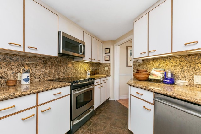 kitchen featuring appliances with stainless steel finishes, dark tile floors, white cabinets, stone countertops, and backsplash